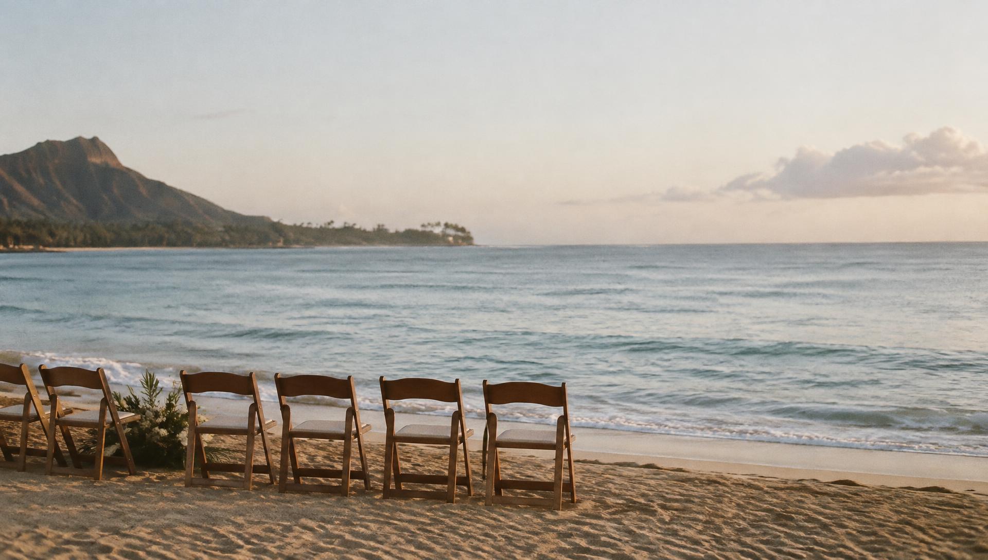 A quiet Oahu shoreline in early morning light with a single row of ceremony chairs facing the water
